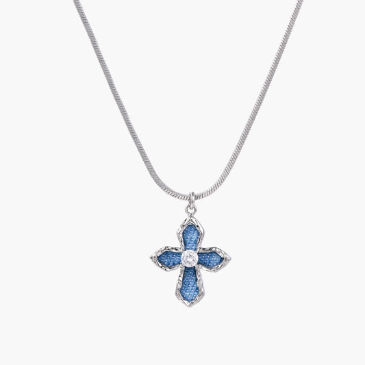 Blue denim-inlaid cross pendant with white gold frame and center zirconia on silver snake chain against cream background