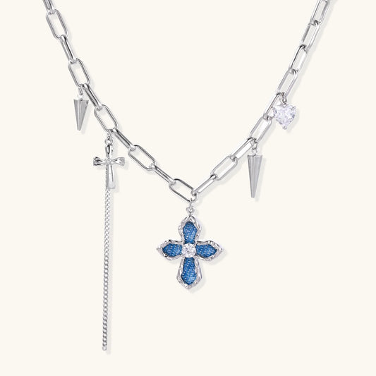 White gold plated chain necklace with blue textured cross pendant, spike charms, and mini cross detail on beige background