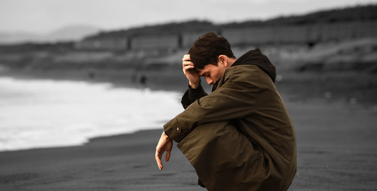 Man depressed on the beach wearing a hoodie