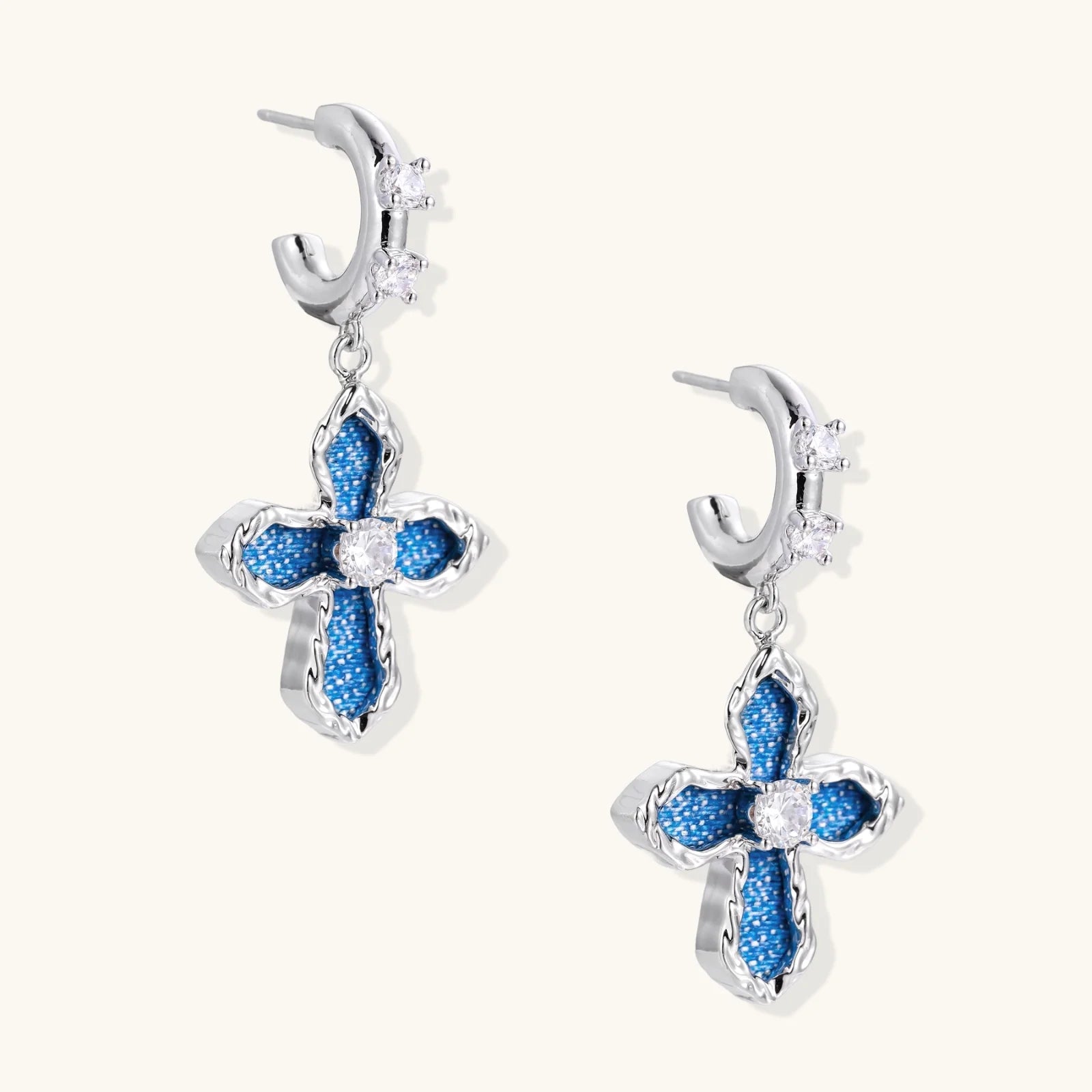 Silver hoops with denim-inlaid cross charms and clear crystals on beige background