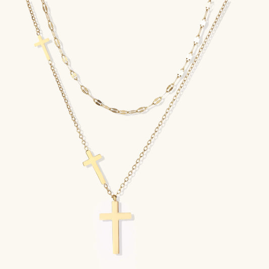 Three-layered gold necklace set with graduated cross pendants in mixed chain styles on white background.